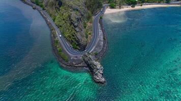 An aerial view captures a winding road as it travels towards the ocean, showcasing the interaction between man-made infrastructure and the natural environment. photo