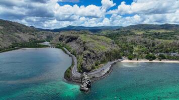 An aerial view captures a winding road as it travels towards the ocean, showcasing the interaction between man-made infrastructure and the natural environment. photo