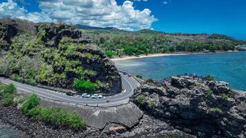 An aerial view captures a winding road as it travels towards the ocean, showcasing the interaction between man-made infrastructure and the natural environment. photo