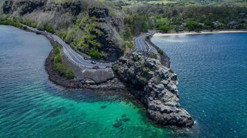An aerial view captures a winding road as it travels towards the ocean, showcasing the interaction between man-made infrastructure and the natural environment. photo