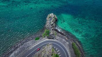 An aerial view captures a winding road as it travels towards the ocean, showcasing the interaction between man-made infrastructure and the natural environment. photo