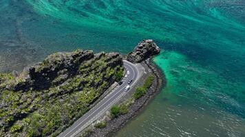 An aerial view captures a winding road as it travels towards the ocean, showcasing the interaction between man-made infrastructure and the natural environment. photo