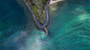 An aerial view captures a winding road as it travels towards the ocean, showcasing the interaction between man-made infrastructure and the natural environment. photo