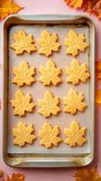 Homemade Maple Leaf Shaped Cookies on Baking Sheet with Fall Foliage Backdrop photo