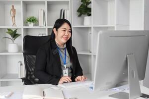 Middle-aged Business Woman Working at Desk in Modern Office Setting with Computer and Shelves in Background photo