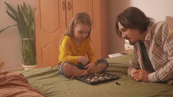 Happy father and little girl enjoy checkers together. video