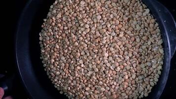 A hand holds the handle of a black frying pan with split peas flying out of the frying pan in super slow motion video