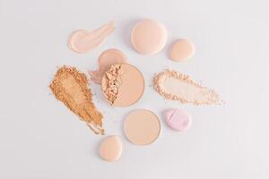 Samples of compact powder and loose powder of different tones, strokes, blocks, sponge on a white background. top view. texture of various powders. photo