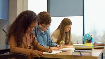 Lesson in class of children, in front girl sitting at desk writing in notebook video