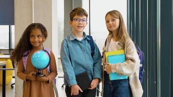 Portrait of three successful diverse pupils with a book and globe in classroom. Back to school video