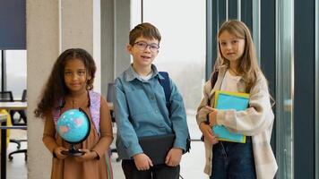 Portrait of three successful diverse pupils with a book and globe in classroom video