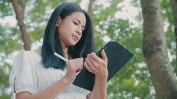 Asian woman write down the ideas on tablet, working remotely, paperless concept for sustainable environment, online applications, online sketch drawing, working with smart technology, modern hand draw video