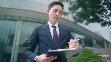White mix race Businessman thinking and writing ideas onto the paper clipping on paperboard standing in front of office building, marketing creative ideas for clients, signing agreement approvement video
