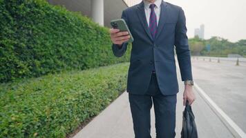 Mid body shot of Young smart businessman in full suits using cellphone while walking to work, scrolling down smartphone business and modern technology, checking work strategy data video