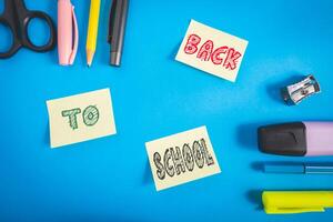 Office and school supplies on a blue background. And three sticky notes with back to school on it. photo