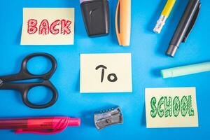 Office and school supplies on a blue background. And three sticky notes with back to school on it. photo