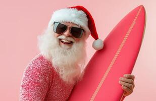 Santa Claus wearing sunglasses, holding a surfboard, smiling on a bright pink background photo