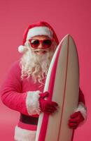 Santa Claus wearing sunglasses, holding a surfboard, smiling on a bright pink background photo