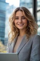 Professional woman smiling with a laptop outside a modern office building during the day photo