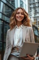 Professional woman smiling with a laptop outside a modern office building during the day photo