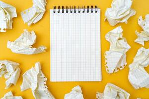 Notepad and crumpled sheets of paper on a yellow background. photo