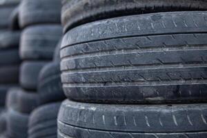 A pile of old tires stacked on top of each other. The tires are black and appear to be worn out. Concept of neglect and abandonment, as the tires are piled up and not being used. photo