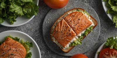 an overhead view of a salmon sandwich on a white plate with lettuce tomato and a gray speckled background. photo