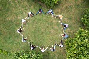 Top view of people standing in circle on green grass doing exercises photo