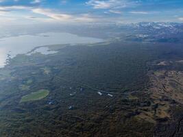 High vantage point captures a vast green landscape in Iceland, featuring a winding road and a distant body of water, likely a lake or fjord. photo