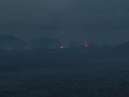 A dark, misty scene in Iceland featuring small, glowing orange lights from volcanic activity. The eerie atmosphere highlights the natural beauty and power of Iceland's landscape. photo
