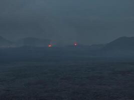 Aerial view of a dark, misty volcanic landscape in Iceland, featuring small glowing red volcanic vents in the distance. Captivating and mysterious scenery. photo