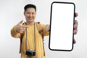 Excited tourist traveling with camera backpack and showing large empty smartphone at camera. Happy male traveler having fun against gray background. photo