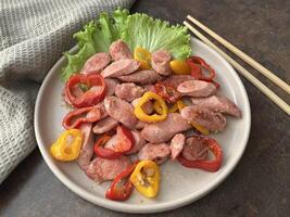 Sauteed sausages with bell peppers served on a plate with green lettuce on a rustic table with chop stick. Close up photo