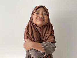Expressive Asian Muslim little girl wearing hijab put both hands in front of the body with a sad face. Unpleasant gesture photo
