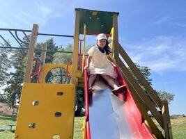 Happy Asian little girl playing slide in playground. Kids having fun in playground. photo