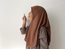 Asian Muslim little girl wearing hijab show a gesture of pointing at something by facing sideways photo
