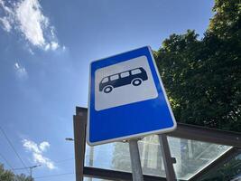 Bus stop sign with bus stop roof, leaves and blue sky in the background photo