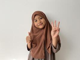 Asian Muslim little girl wearing hijab smiling at the camera show thumbs up gesture. photo