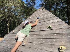 An active little Asian girl is happily playing wall climbing in playground. Bottom view photo