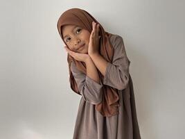 Asian Muslim little girl wearing hijab show cute face with both hands are on the chin photo