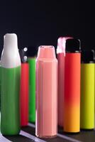 A set of colorful disposable electronic cigarettes of different shapes on a black background with smoke. Concept of modern smoking, vaping and nicotine. photo