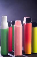 A set of colorful disposable electronic cigarettes of different shapes on a black background with smoke. Concept of modern smoking, vaping and nicotine. photo