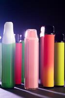 A set of colorful disposable electronic cigarettes of different shapes on a black background with smoke. Concept of modern smoking, vaping and nicotine. photo