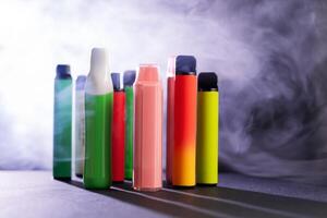 A set of colorful disposable electronic cigarettes of different shapes on a black background with smoke. Concept of modern smoking, vaping and nicotine. photo