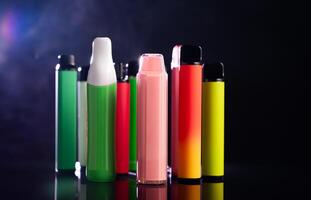 A set of colorful disposable electronic cigarettes of different shapes on a black background with smoke. Concept of modern smoking, vaping and nicotine. photo