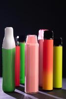A set of colorful disposable electronic cigarettes of different shapes on a black background with smoke. Concept of modern smoking, vaping and nicotine. photo