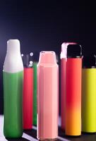 A set of colorful disposable electronic cigarettes of different shapes on a black background with smoke. Concept of modern smoking, vaping and nicotine. photo