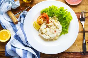 a plate with shrimp, lettuce and lemon on a wooden table photo