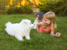 Little smiling girl playing with Samoyed puppy in the summer garden photo