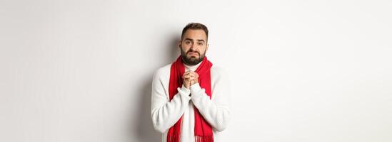 Christmas holidays and New Year concept. Sad man begging for help, holding hands in pray and looking distressed at camera, asking for favour, standing over white background photo